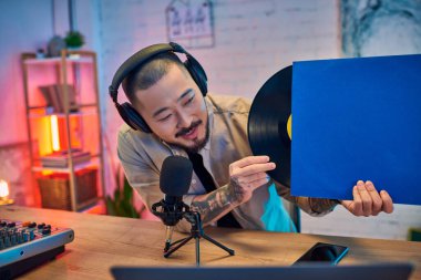 Sakallı ve kulaklıklı genç bir Asyalı stüdyosunda bir podcast kaydediyor..