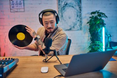 Ev stüdyosunda yakışıklı bir Asyalı elinde plak tutarken podcast yapıyor..