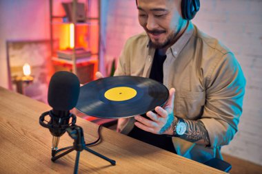 Ev stüdyosunda kulaklık takan Asyalı bir adam podcast yaparken plak kaydı tutuyor..