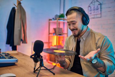 Yakışıklı Asyalı bir adam stüdyosunda bir podcast kaydediyor. Elinde vinil plak tutuyor ve mikrofona hevesle konuşuyor..
