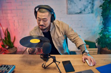 Stüdyoda kulaklıklı bir adam, bir podcast kaydederken vinil plak tutuyor..