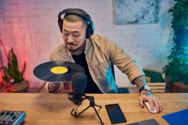 A man with headphones in his studio, holding a vinyl record while recording a podcast. clipart