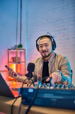Ev stüdyosunda podcast yaparken gülümseyen kulaklık takan yakışıklı bir Asyalı..