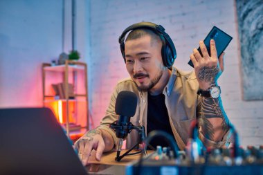 Kulaklık takan Asyalı bir adam podcast yaparken mikrofona konuşuyor..