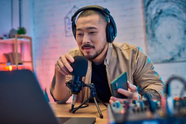 A handsome Asian man records a podcast in his home studio. clipart