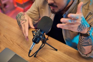 Dövmeli bir adam kendi stüdyosunda bir podcast kaydediyor..