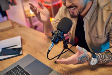 Asyalı bir adam stüdyoda bir podcast kaydediyor, coşkuyla mikrofona konuşuyor..