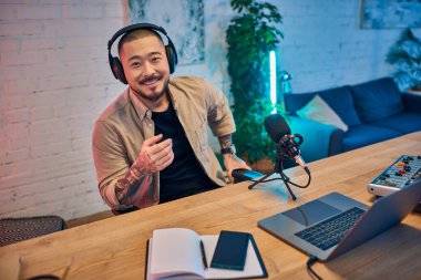 Kulaklık takan gülümseyen Asyalı bir adam stüdyoda bir podcast kaydediyor..