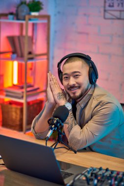 Ev stüdyosunda podcast yaparken gülümseyen kulaklık takan yakışıklı bir Asyalı..