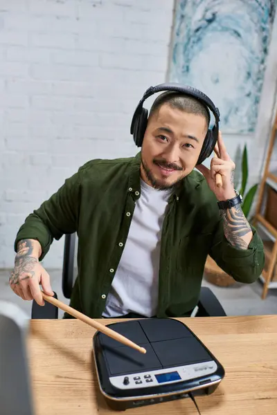 stock image A smiling Asian man with tattoos plays an electronic drum pad in a studio.