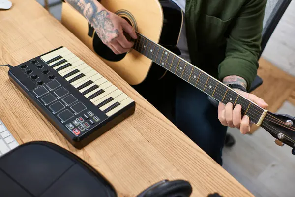 Genç bir Asyalı akustik gitar ve stüdyo ortamında MIDI klavye çalıyor..