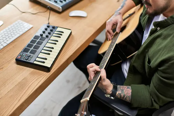 stock image A handsome Asian man plays an acoustic guitar in his studio, surrounded by musical equipment.