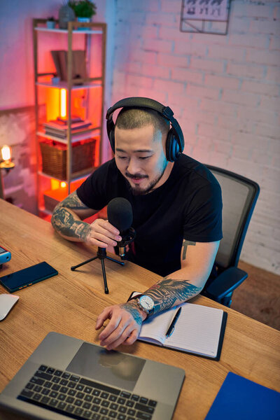 Красивый азиат в наушниках записывает подкаст в своей домашней студии.