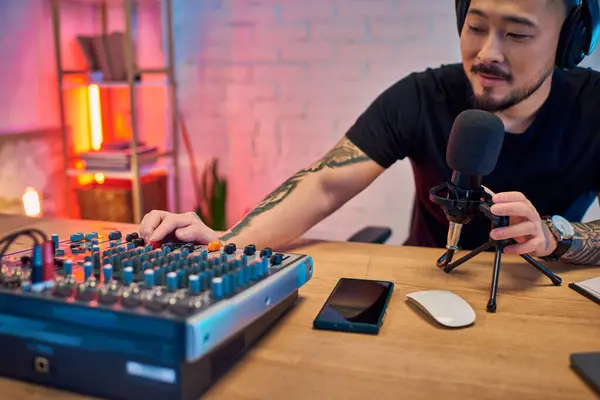 stock image An Asian man records a podcast in his home studio, using a microphone and audio mixer.