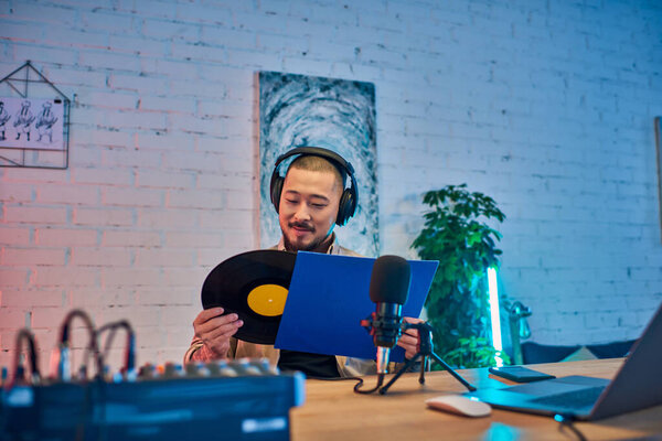 Человек в наушниках держит виниловую пластинку и сценарий во время записи подкаста в своей студии.