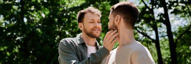 A bearded gay couple enjoys a sunny day in the park, sharing a tender moment of affection. clipart