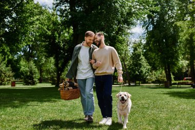 Sakallı eşcinsel bir çift labrador av köpeğiyle yeşil bir parktan geçiyor. İkisi de gülümsüyor ve birbirlerine eşlik etmekten zevk alıyor gibi görünüyorlar..