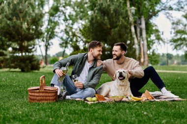 Two bearded men enjoy a picnic with their labrador dog in a green park. clipart