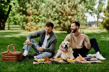 Sakallı eşcinsel bir çift labrador köpeğiyle yemyeşil bir parkta pikniğin tadını çıkarıyor. Çift gülüyor ve bir şişe şarabın tadını çıkarıyor, mutlu ve rahat bir atmosfer yaratıyor..
