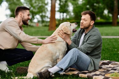 Sakallı eşcinsel bir çift, labrador av köpeğiyle yeşil bir parkta pikniğin tadını çıkarıyor..