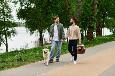 İki sakallı eşcinsel, labrador köpeğiyle yeşil bir parkta el ele yürür ve pikniğin tadını çıkarırlar..