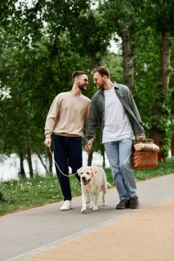 Sakallı eşcinsel bir çift labrador köpeğiyle yeşil bir parkta pikniğin tadını çıkarıyor..
