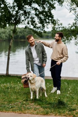 İki sakallı adam labrador köpeğiyle parkta piknik yapıyor..
