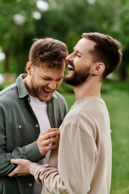 Two bearded men laugh together in a green park, enjoying a sunny afternoon. clipart