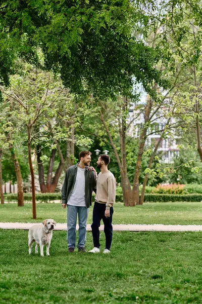 stock image A bearded gay couple in casual attire enjoys a sunny afternoon in the park with their labrador retriever.