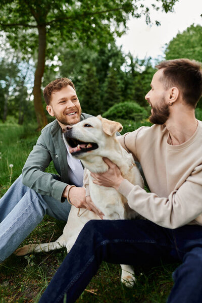 A bearded gay couple enjoys a day out in a green park with their labrador retriever.