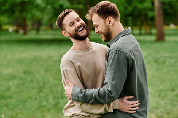 A bearded gay couple shares a moment of laughter and affection while enjoying a sunny day in a green park.