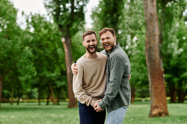 A bearded gay couple happily embraces in a lush green park, their laughter echoing through the trees.