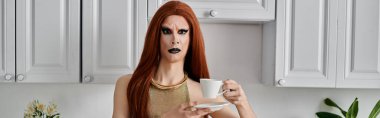 Büyüleyici kıyafetli bir travesti mutfakta bir fincan kahveden zevk alır..