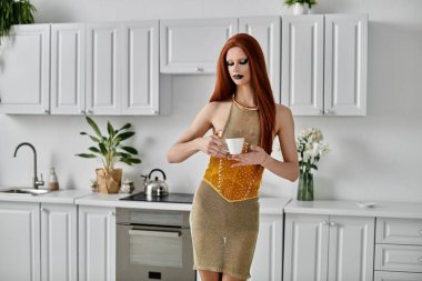 Şık bir travesti modern bir mutfakta bir fincan çayla poz verir..