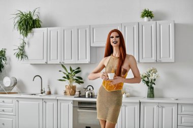 A drag queen in a sparkly gold dress enjoys a cup of coffee in a stylish kitchen. clipart