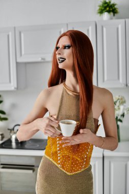 Bir drag diva şık bir altın elbise giyerken bir fincan kahvenin tadını çıkarır..