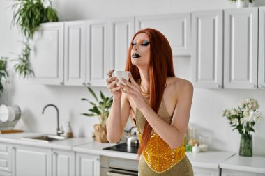 Göz kamaştırıcı bir travesti şık bir mutfak ortamında bir fincan çay içer..
