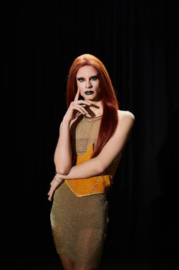 Bir travesti, kendine güveni ve tarzını gösteren göz kamaştırıcı bir altın elbiseyle poz verir..