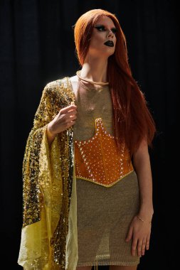 A glamorous drag queen in a gold sequined shawl and a shimmering, orange jeweled corset poses in a dramatic pose. clipart