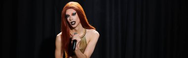 Gösterişli altın kıyafetli bir drag diva sahnede bir mikrofon tutuyor..