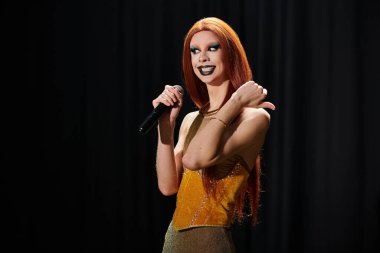 Altın elbiseli bir drag diva sahnede bir mikrofon tutuyor..