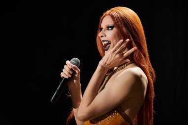 Drag Queen sahnede, elinde mikrofonla, yüzünde dramatik bir ifadeyle..