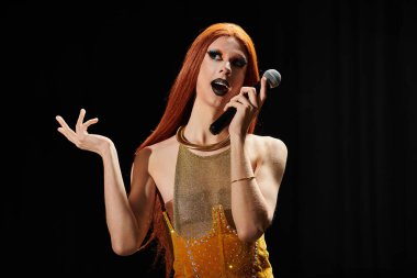 Uzun kızıl saçlı bir travesti sahnede mikrofon tutuyor..
