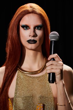 Altın zincirli bir bluz giyen bir travesti mikrofonu elinde tutuyor..