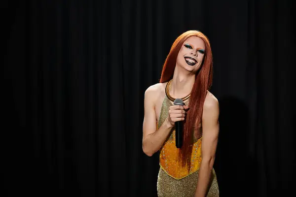 stock image A drag queen in a gold sequined dress smiles brightly while holding a microphone.