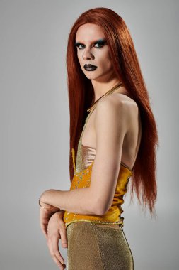 Bir travesti göz alıcı altın bir elbise içinde cesur bir makyajla poz verir..