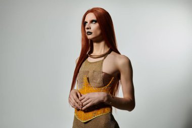 Göz kamaştırıcı bir travesti, kendine güvenen bir stüdyoda, pırıl pırıl, altın bir elbise sergiliyor..