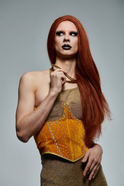 Işıldayan altın bir elbise giymiş bir travesti büyüleyici bir poz verir..