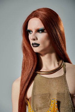 A glamorous drag queen with long red hair poses in a gold mesh top. clipart