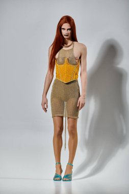 Işıldayan altın kıyafetli çekici bir travesti beyaz bir fonda poz veriyor..